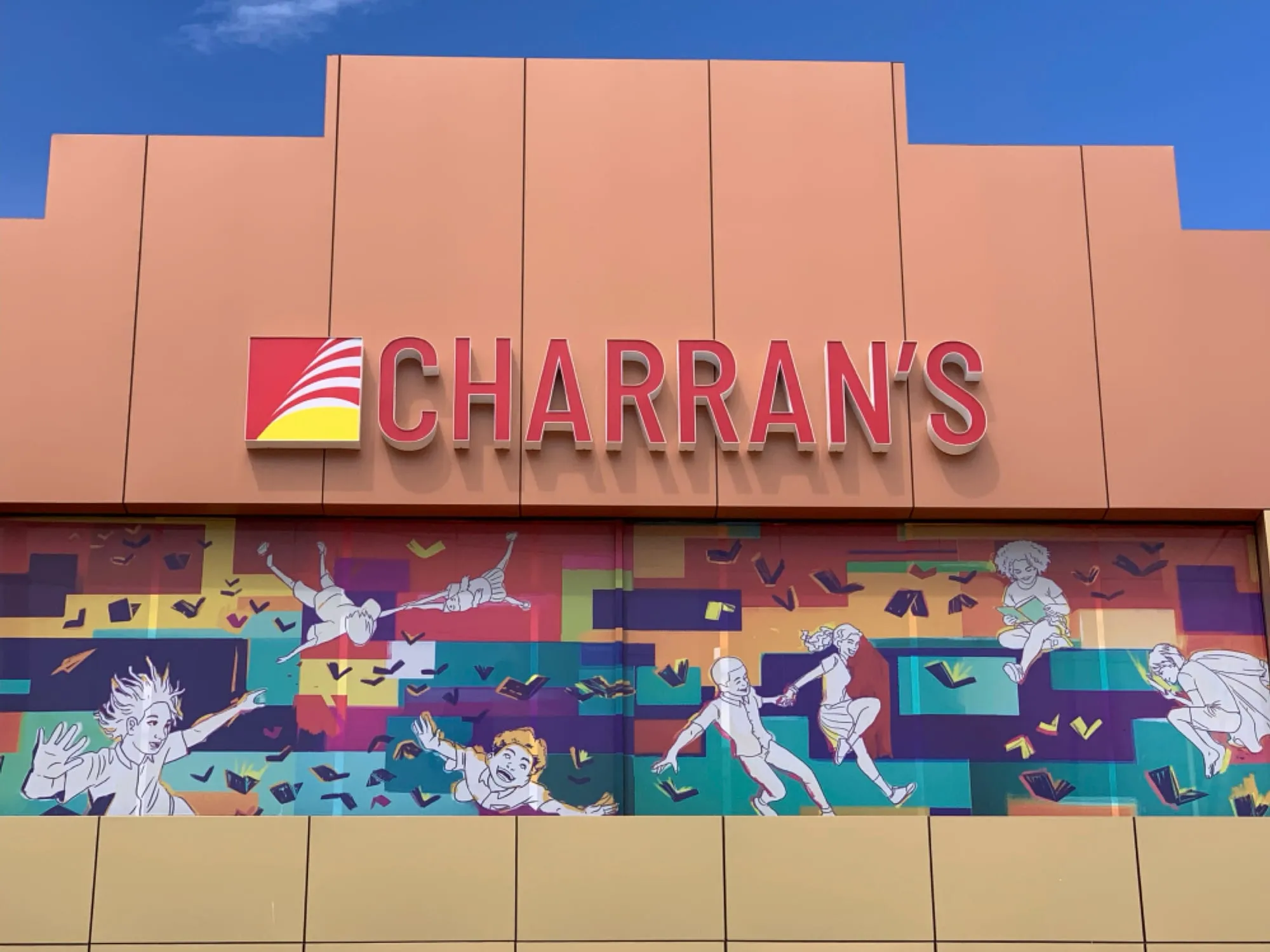 Charran's storefront: a 40ft mural of figures leaping among flying books in blocks of teal, purple and orange, beneath the Charran's sign.